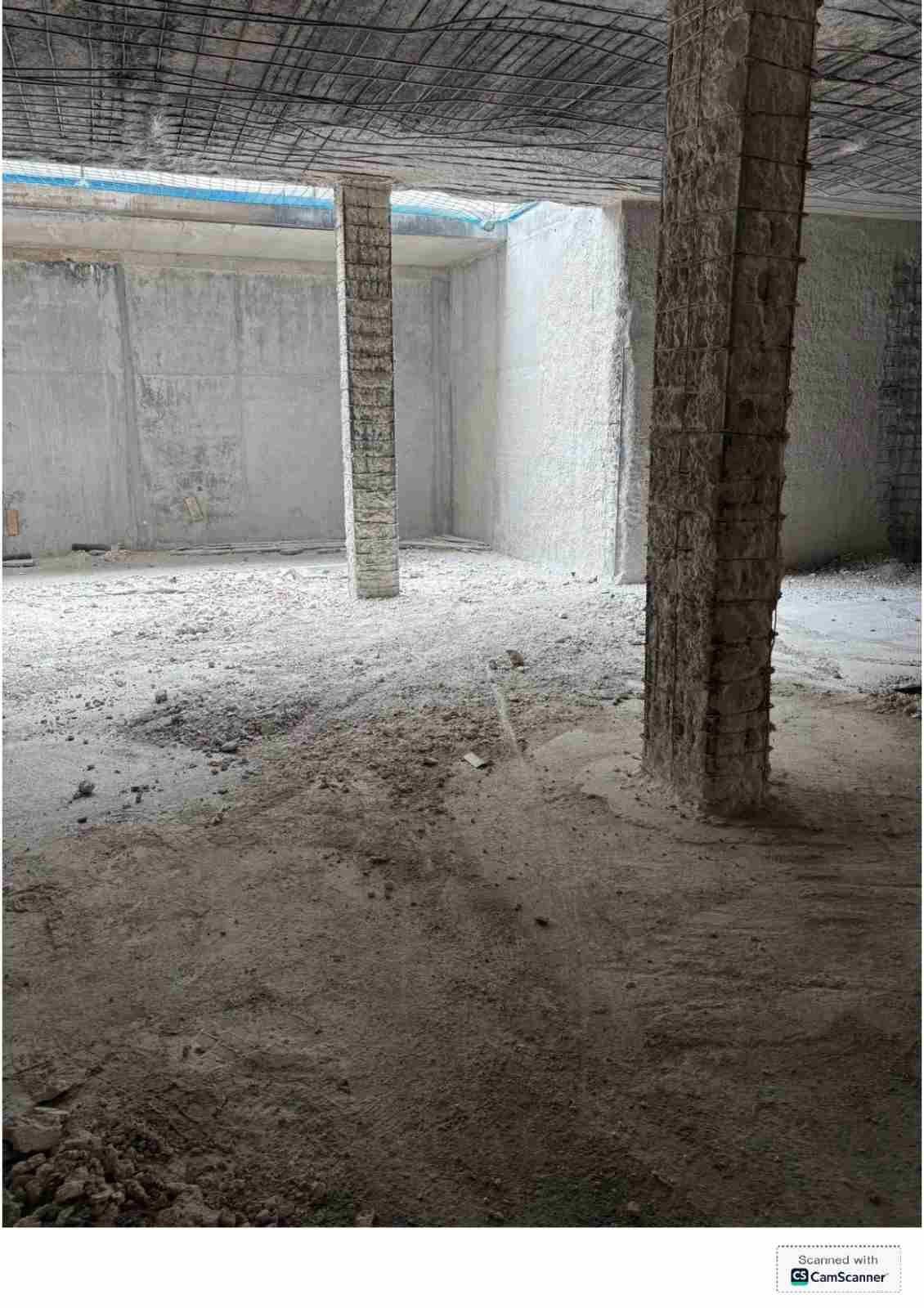 Habitación de hormigón sin terminar, con columnas, el suelo cubierto de polvo y una pequeña abertura de ventana en la pared.
