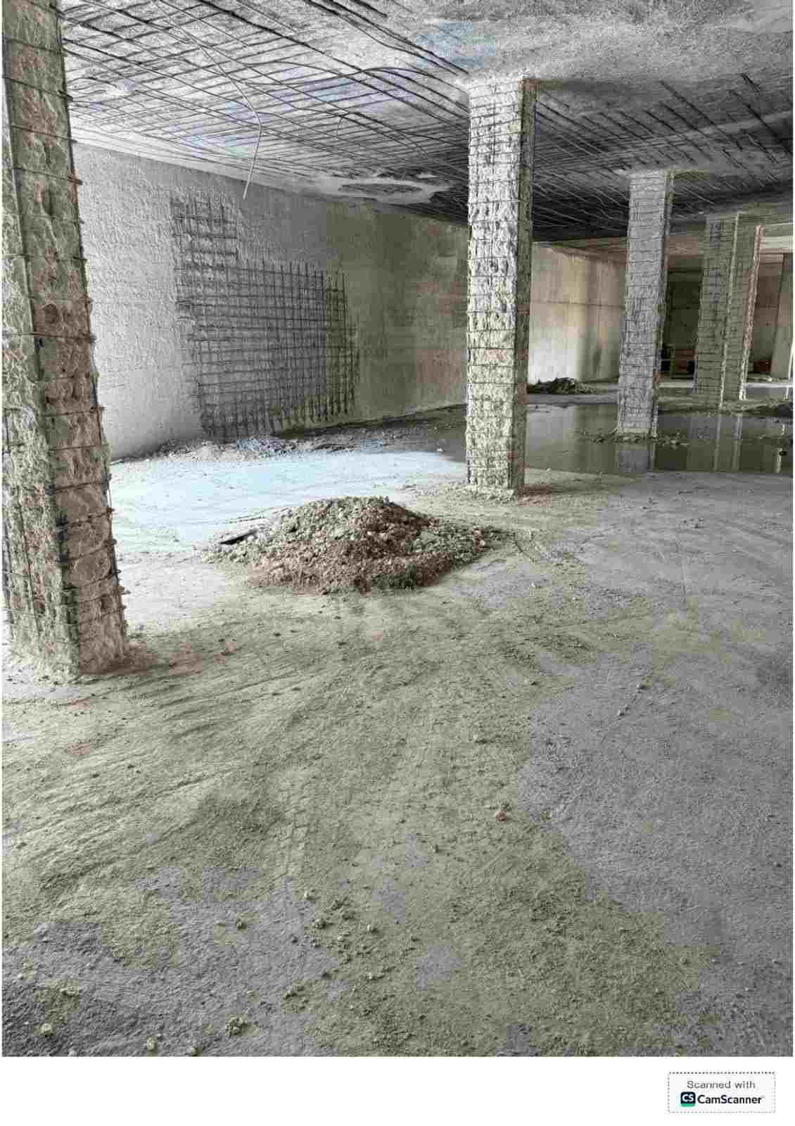 Habitación de hormigón vacía e inacabada, con pilares de soporte y un montón de escombros en el suelo.