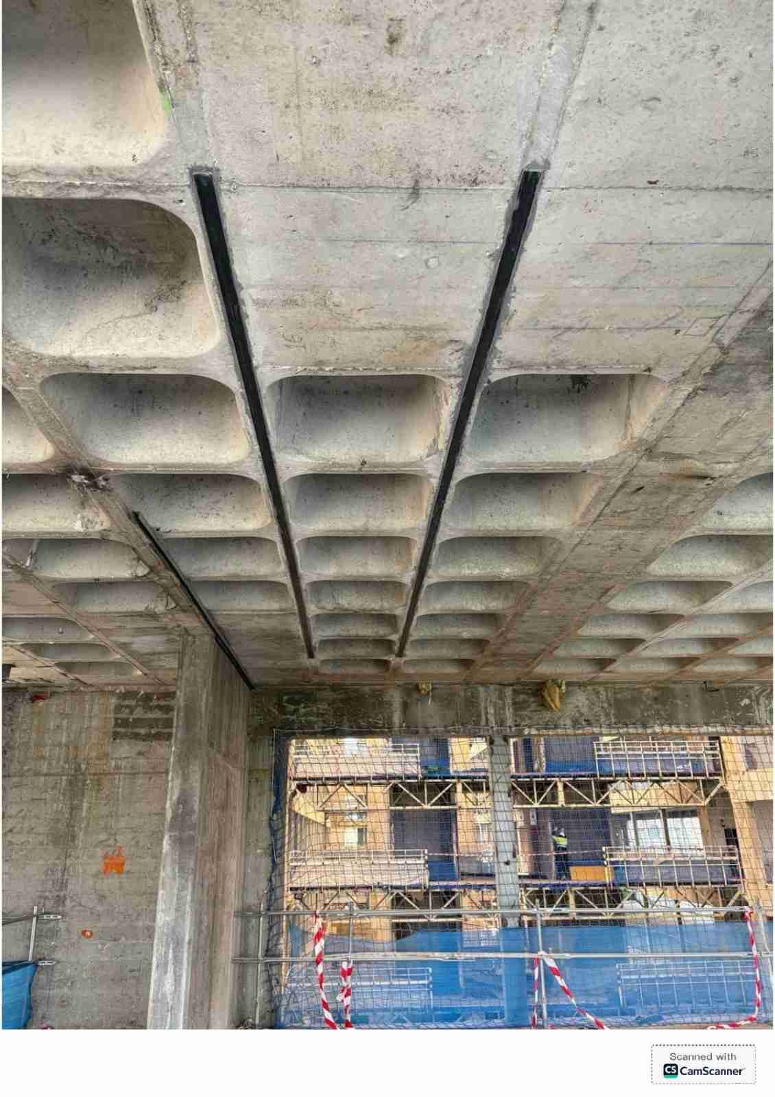 Parte inferior de un puente de hormigón o paso elevado en construcción, con andamios y redes de seguridad debajo.