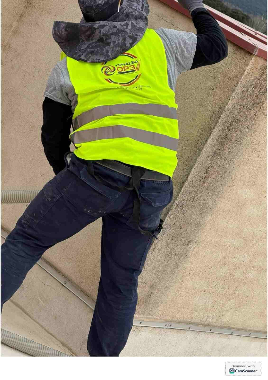 Trabajador con chaleco de seguridad amarillo neón trepando por un muro de hormigón empinado al aire libre