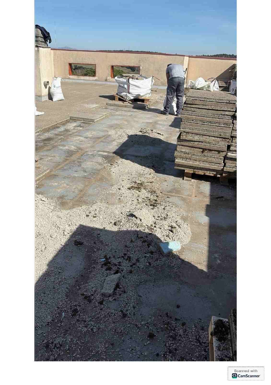 Obreros de la construcción en una azotea, con materiales apilados y una superficie gris sin terminar bajo un cielo despejado