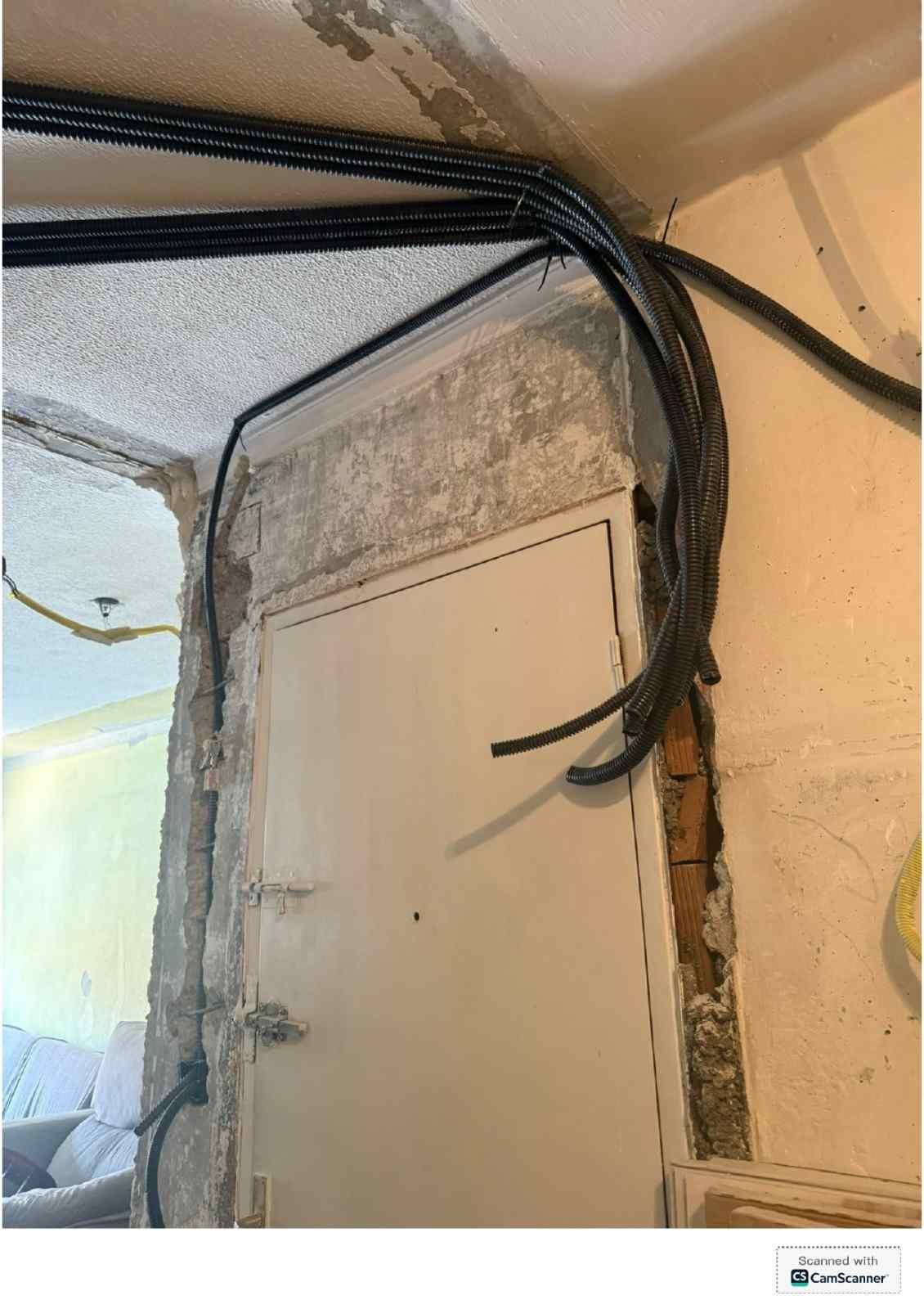 Haces de cables negros recorren una pared y el marco de una puerta, cerca del techo, en un espacio interior sin terminar