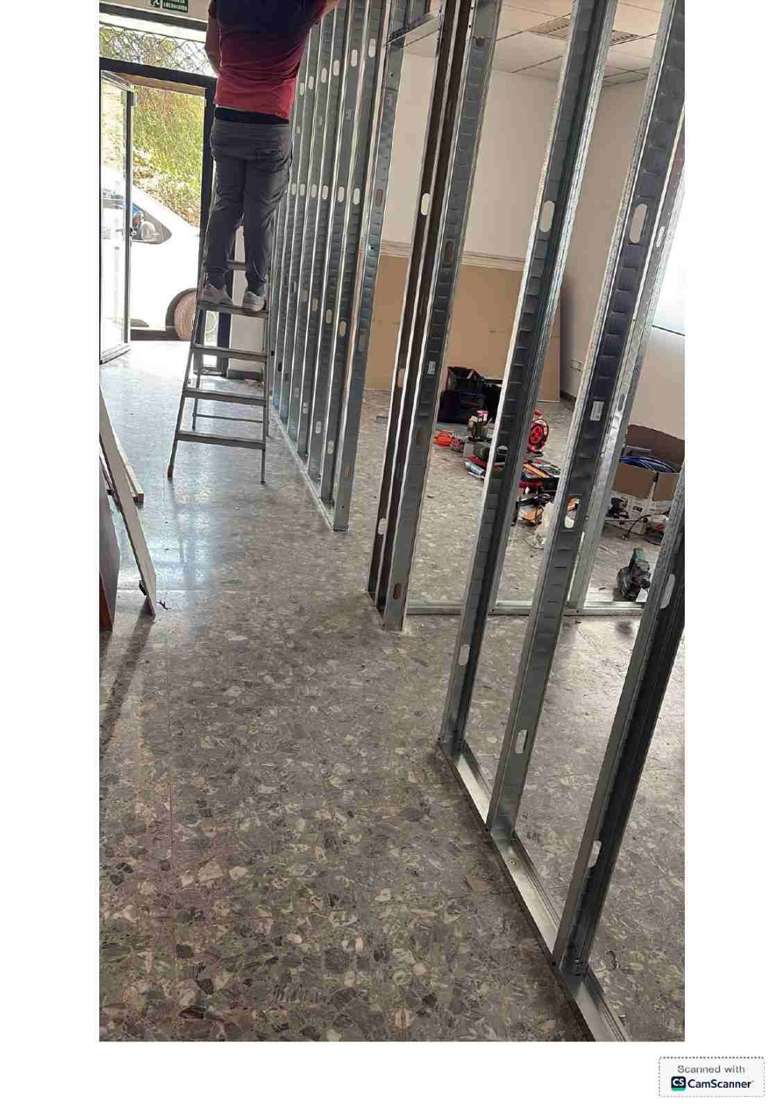 Pasillo estrecho en obras, con la estructura de madera a la vista, una escalera y herramientas en el suelo