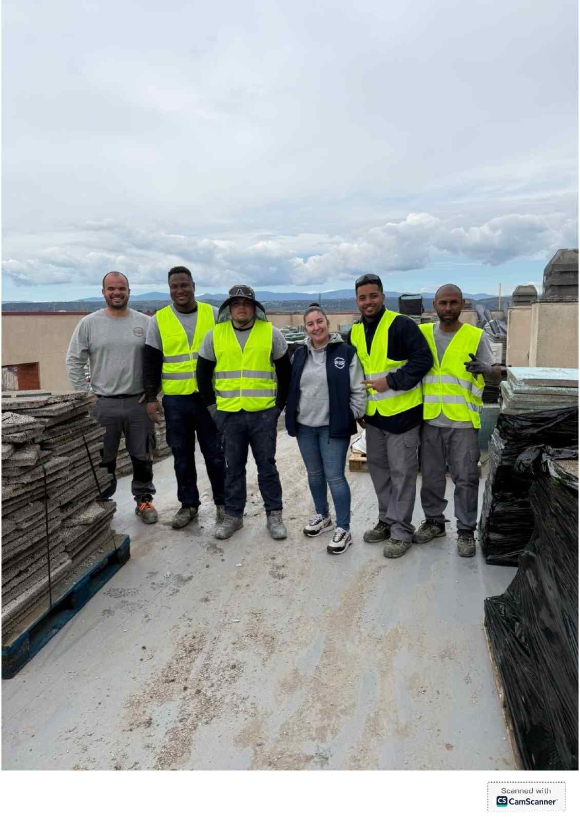 Grupo de trabajadores con chalecos de alta visibilidad en una obra en una azotea, rodeados de materiales apilados