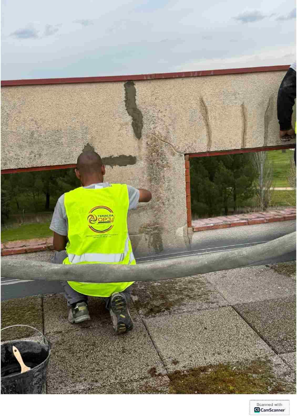 Trabajador con chaleco reflectante reparando con una llana una pared agrietada en la azotea.