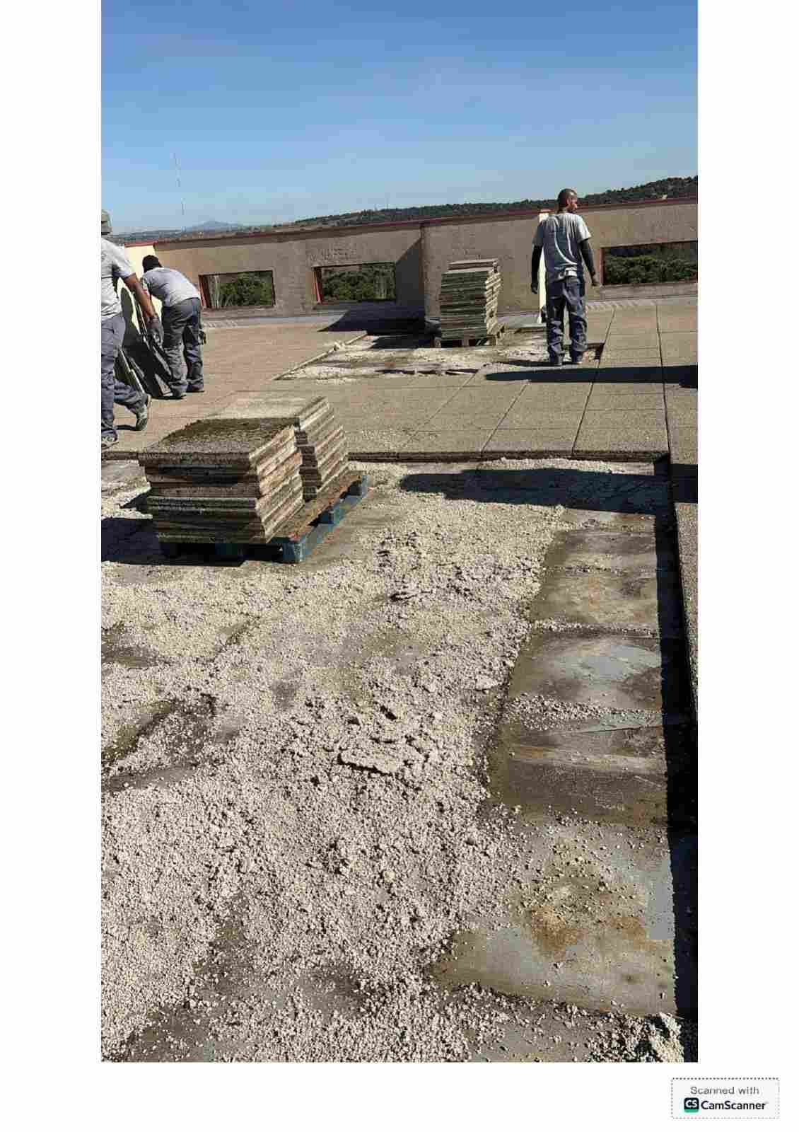 Obreros de la construcción en una azotea, con baldosas apiladas y un cielo azul despejado.