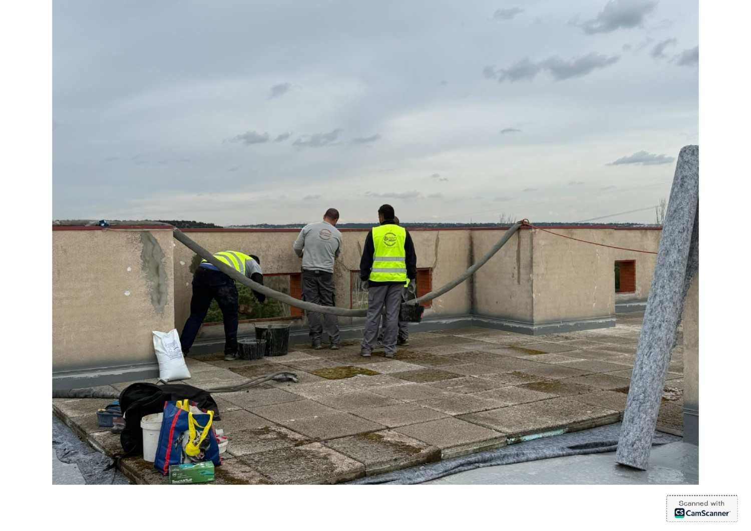 Trabajadores instalando una membrana para techos en una azotea plana bajo un cielo nublado