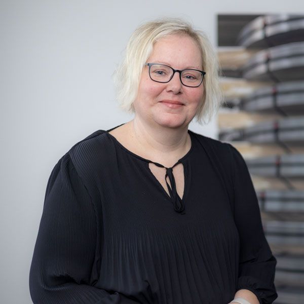 Eine Frau mit Brille und blauem Hemd lächelt in die Kamera.