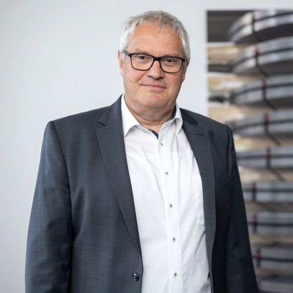 Ein Mann mit Brille und blau kariertem Hemd lächelt in die Kamera.