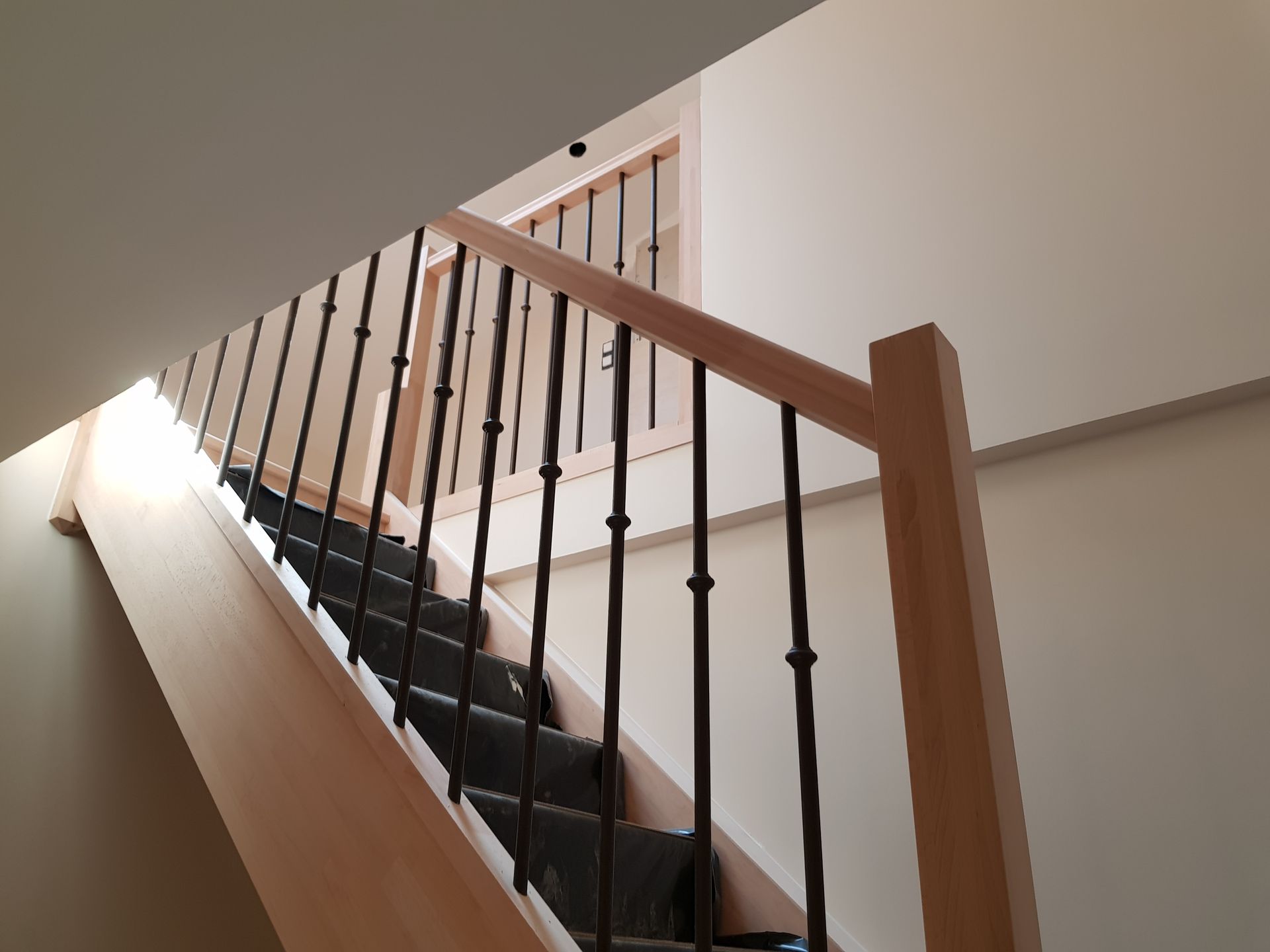 Rambarde d'escalier en bois à côté d'une fenêtre sombre dans une cage d'escalier intérieure étroite.