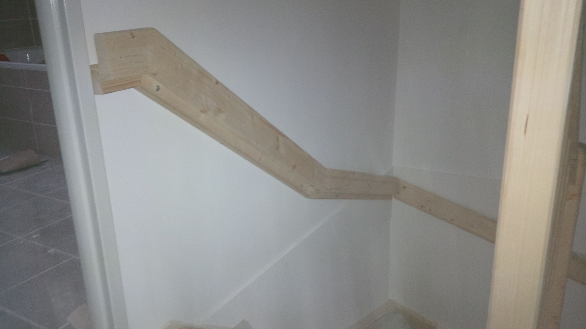 Rambarde en bois fixée le long d'un mur de cage d'escalier dans un couloir intérieur blanc.