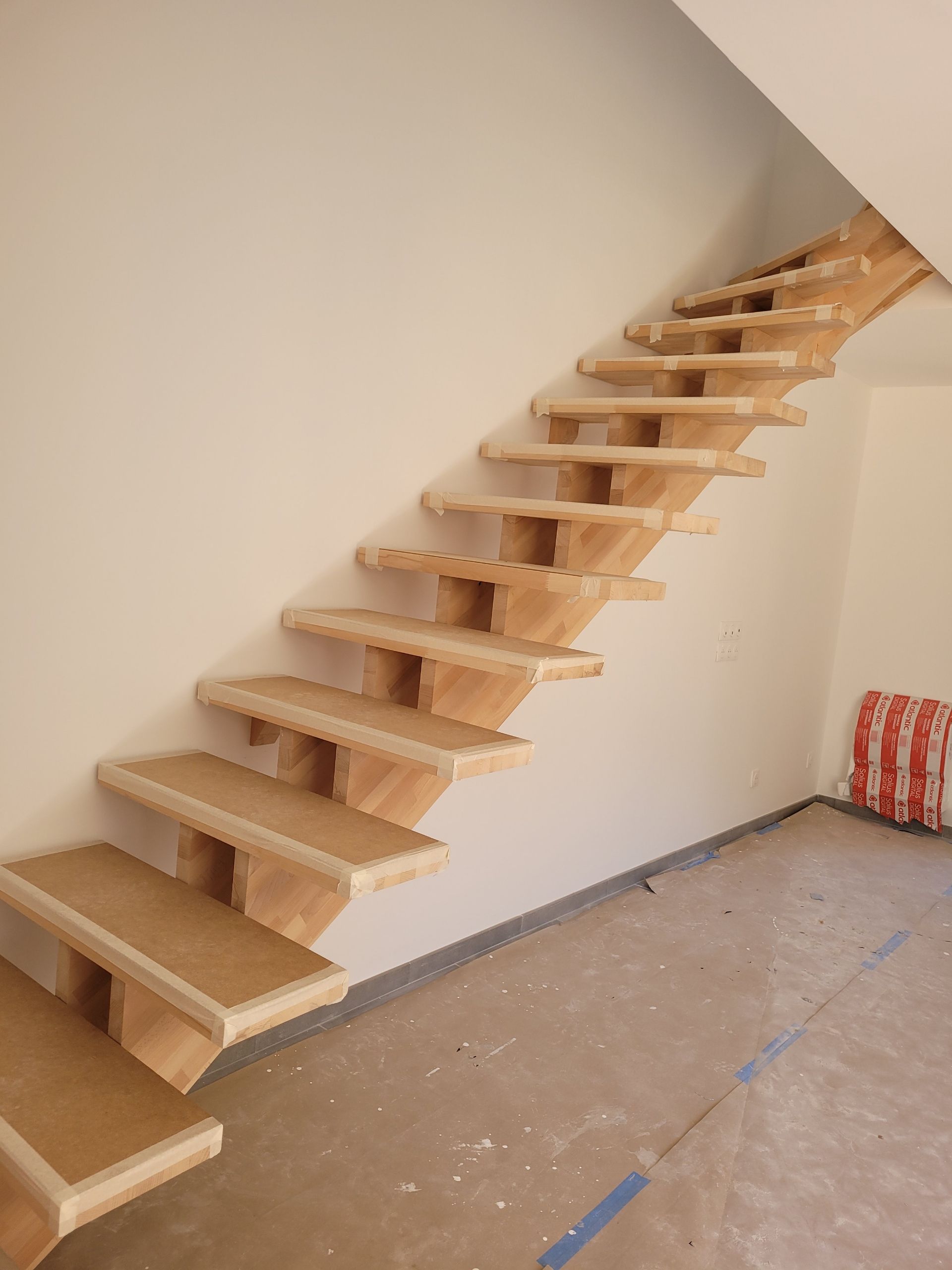 Escalier en bois suspendu le long d'un mur beige dans une pièce inachevée.