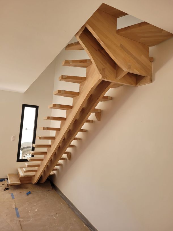 Escalier en bois en construction le long d'un mur incliné dans une pièce nue avec une fenêtre étroite.