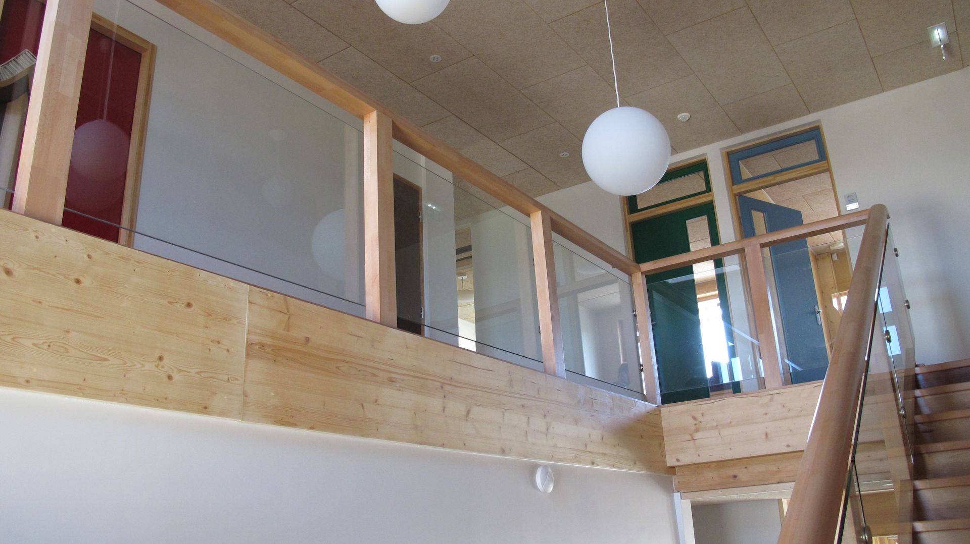 Balcon intérieur lumineux avec balustrade en bois, suspensions lumineuses et escalier sur la droite