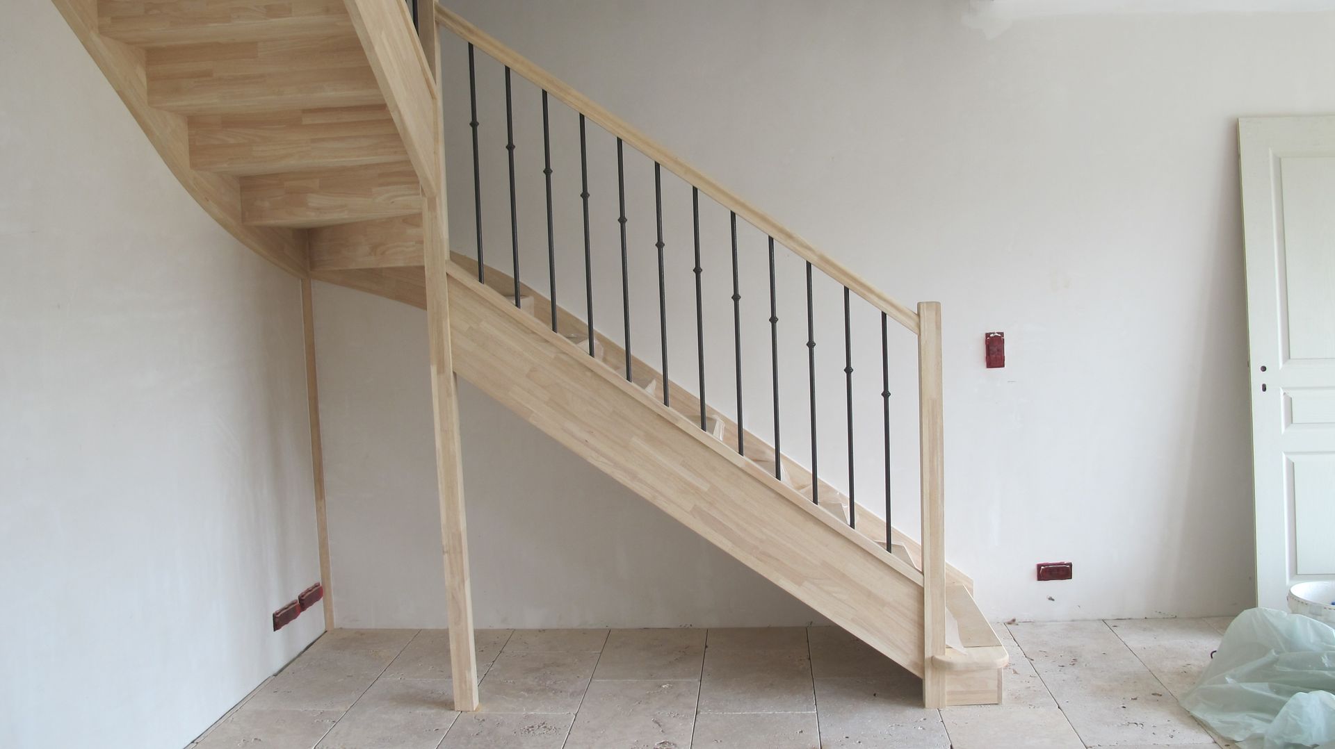 Escalier intérieur en construction avec marches en bois clair et rampe noire dans une pièce inachevée
