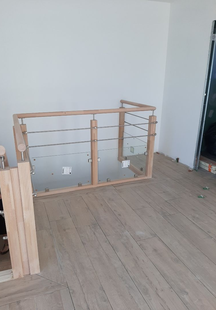 Rambarde d'escalier intérieure avec poteaux en bois clair et pièces métalliques dans une pièce peu aménagée.