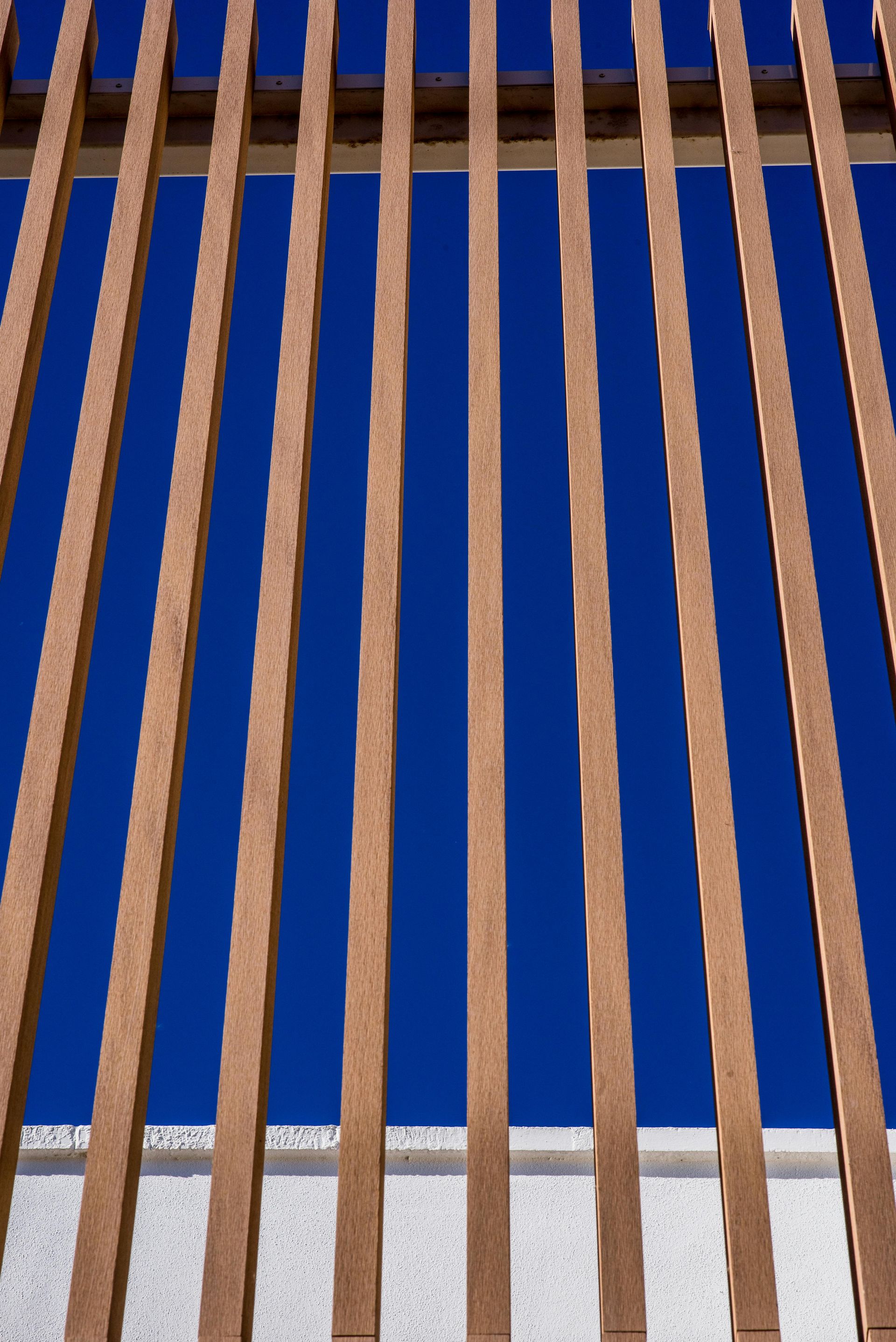 Lattes de clôture en bois se détachant sur un ciel d'un bleu profond, au-dessus d'un mur blanc.