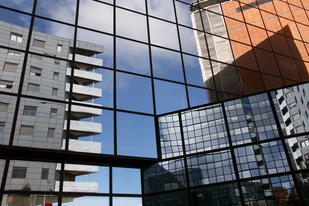 Façade d'un bâtiment recouvert de vitres où l'on peut voir  le reflet d'un grand immeuble gris de plusieurs étages