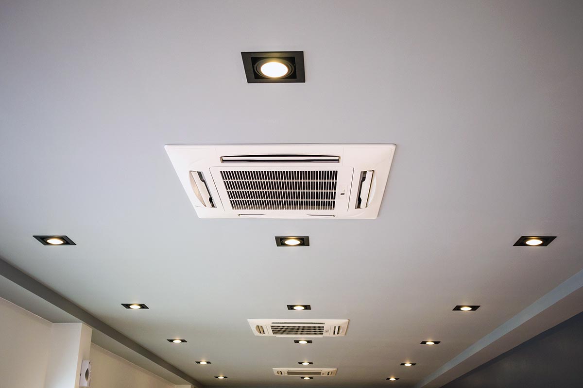 Plusieurs climatisations cassettes fixées au plafond le long d'un grand couloir éclairé de spots lumineux.