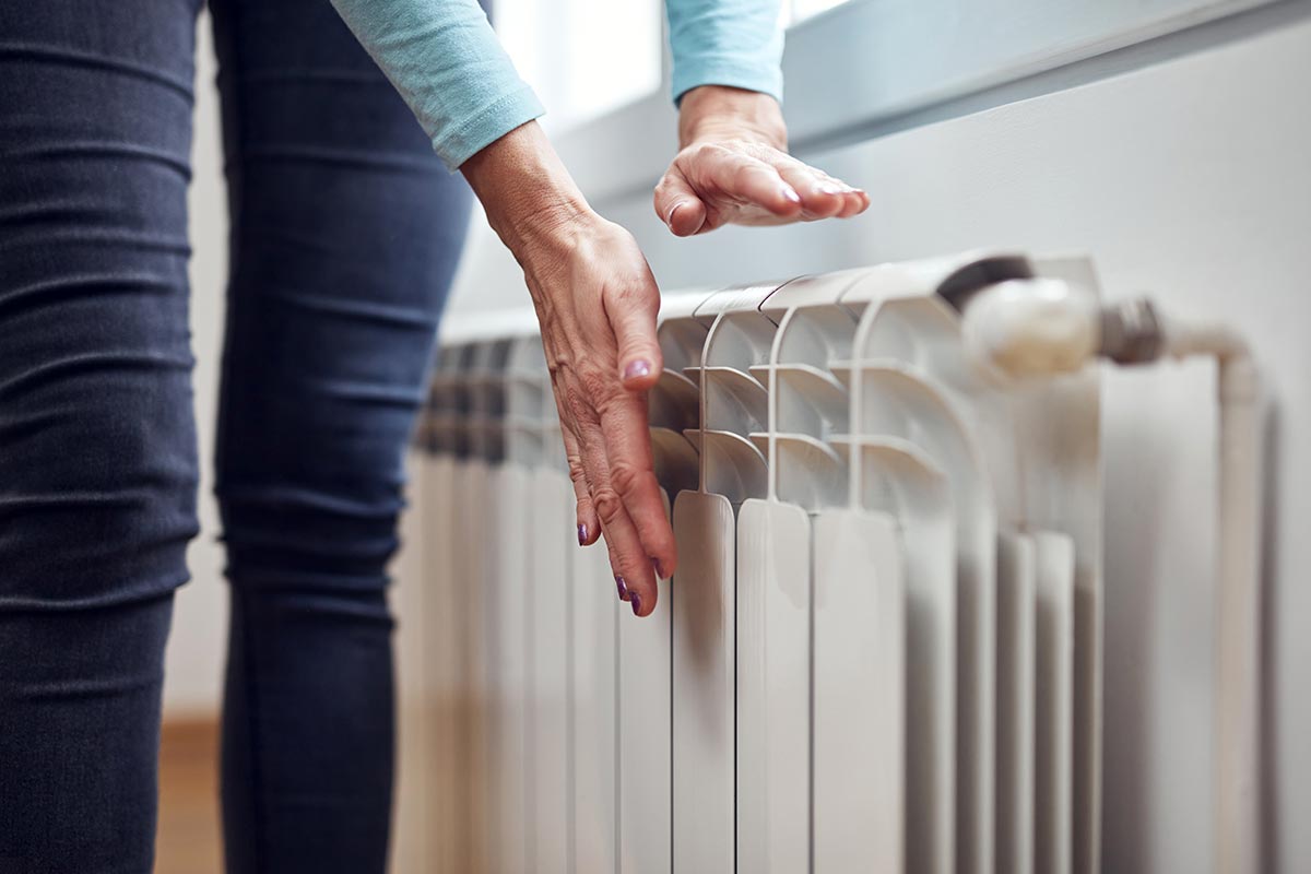 Une dame en train de vérifier avec les paumes de ses mains si son radiateur émet de la chaleur