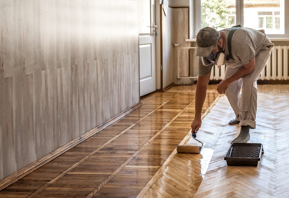 Ein Mann streicht einen Holzboden mit einer Rolle.