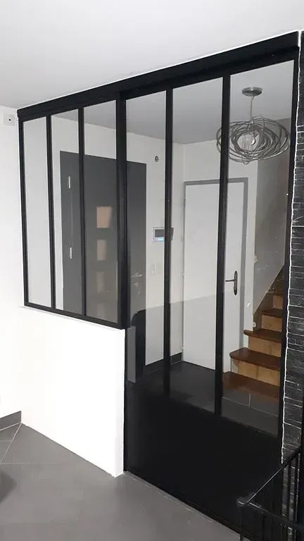 Grande verrière noire entre les escaliers et un salon