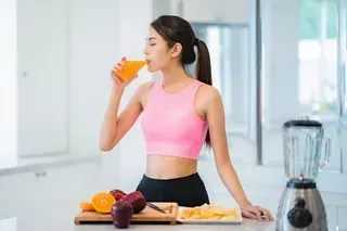 Una mujer está bebiendo jugo de naranja en una cocina.