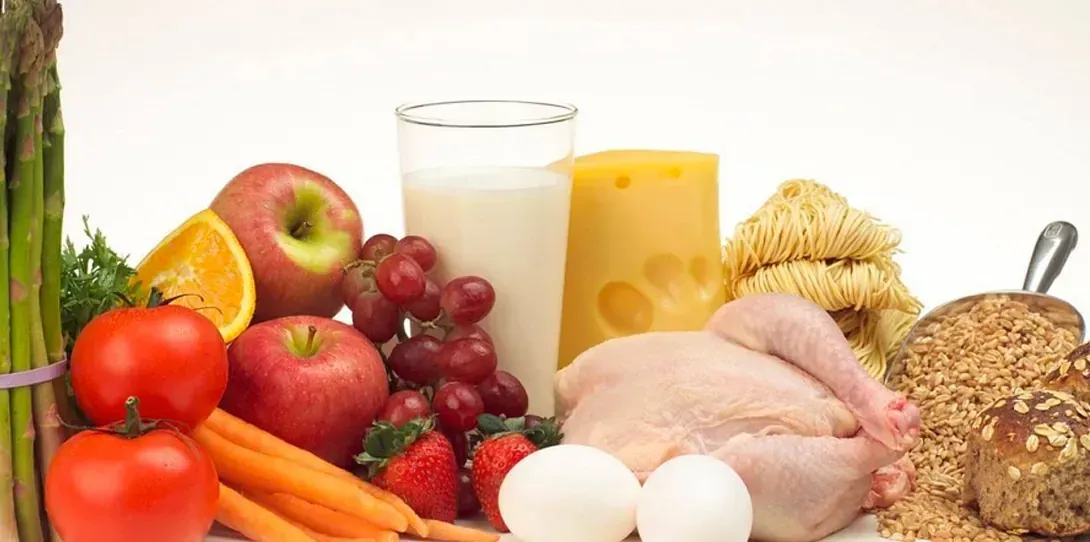 Una variedad de alimentos saludables que incluyen frutas, verduras, huevos, leche y pan en una mesa.