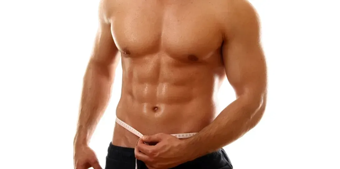 Un hombre sin camisa mide su cintura con una cinta métrica.