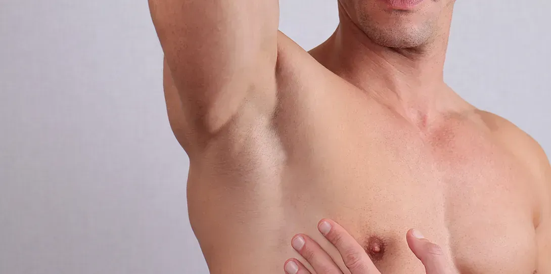 Un hombre sin camisa se mira la axila.