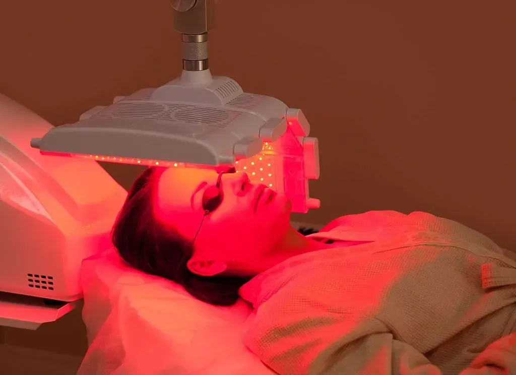Una mujer recibe un tratamiento de luz roja en su cara.