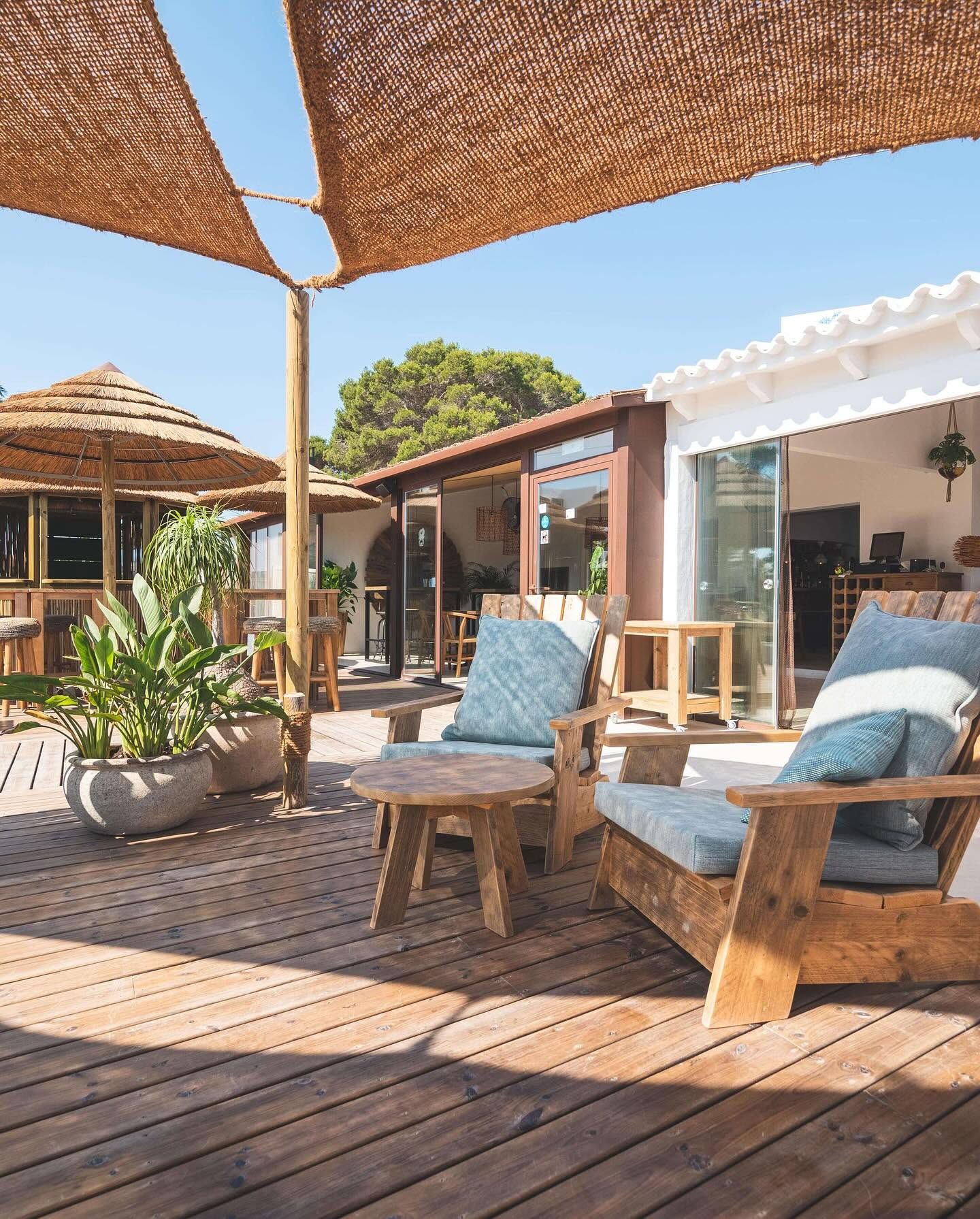 Patio soleado con sillas de mimbre, mesa de madera y toldos en el exterior de una casa moderna.