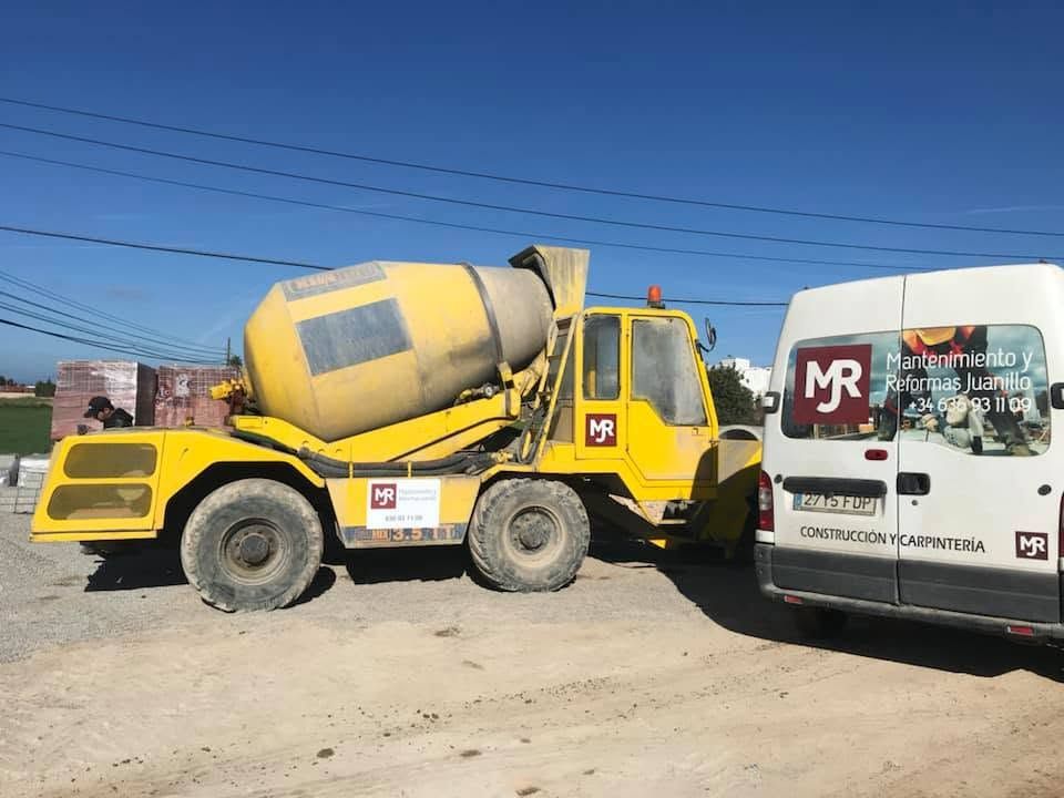 Un camión hormigonera amarillo aparcado junto a una furgoneta blanca bajo un cielo azul despejado.