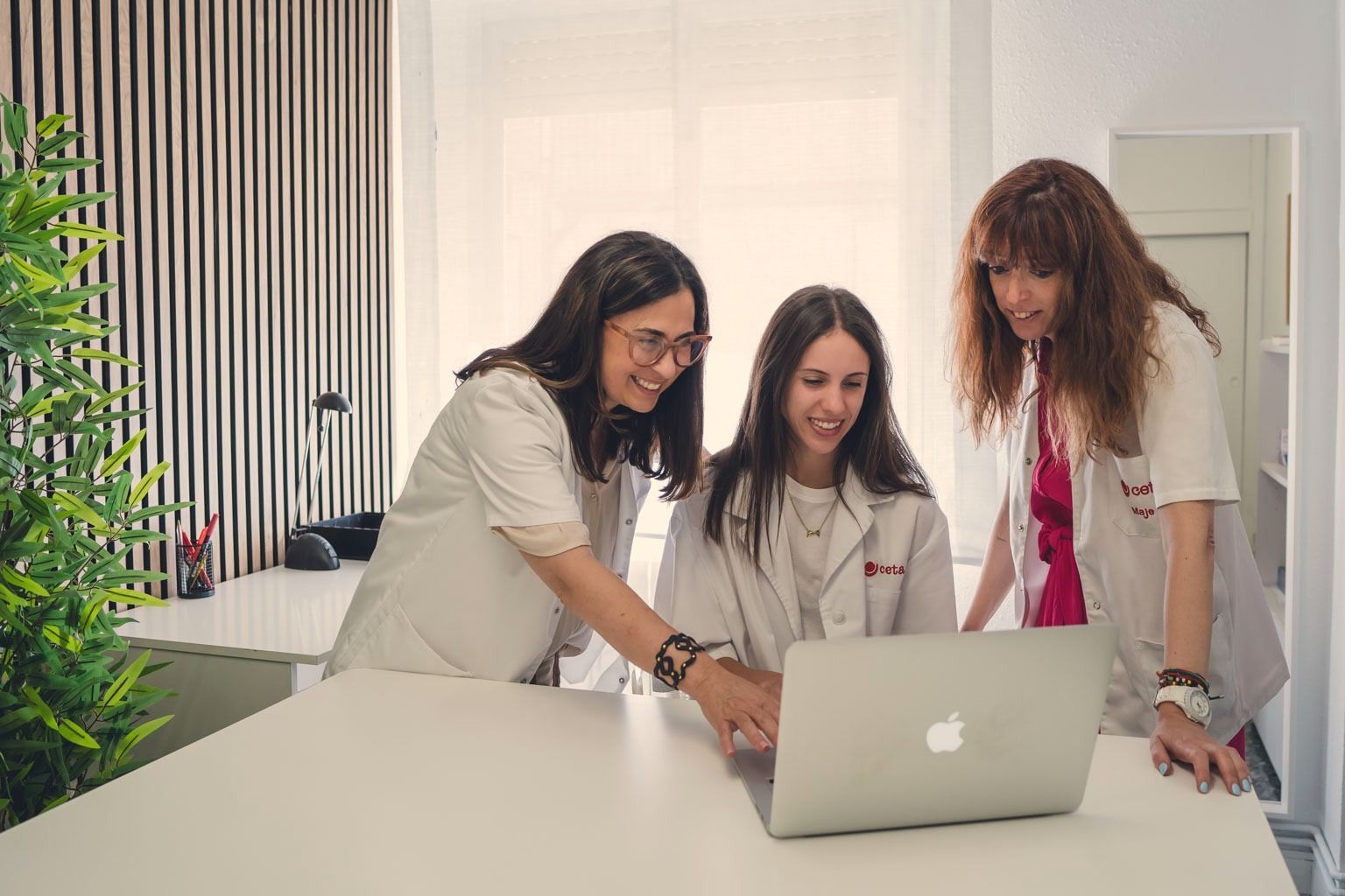 Tres mujeres están de pie alrededor de una mesa mirando una computadora portátil.