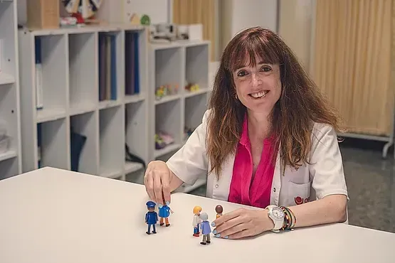Una mujer está sentada en una mesa jugando con figuras de juguete.
