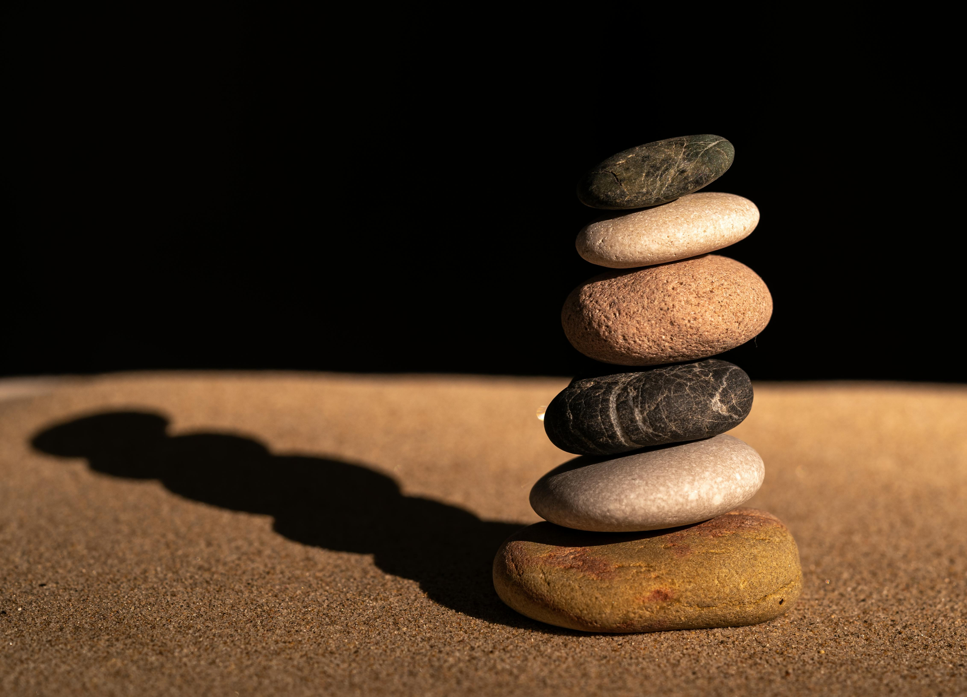 Pila de guijarros equilibrados que proyectan largas sombras sobre una superficie arenosa.