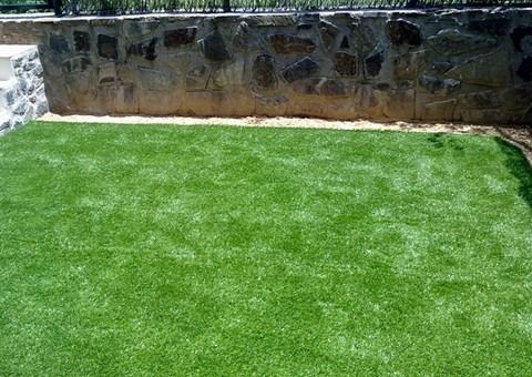 Un césped verde y exuberante con un muro de piedra al fondo.
