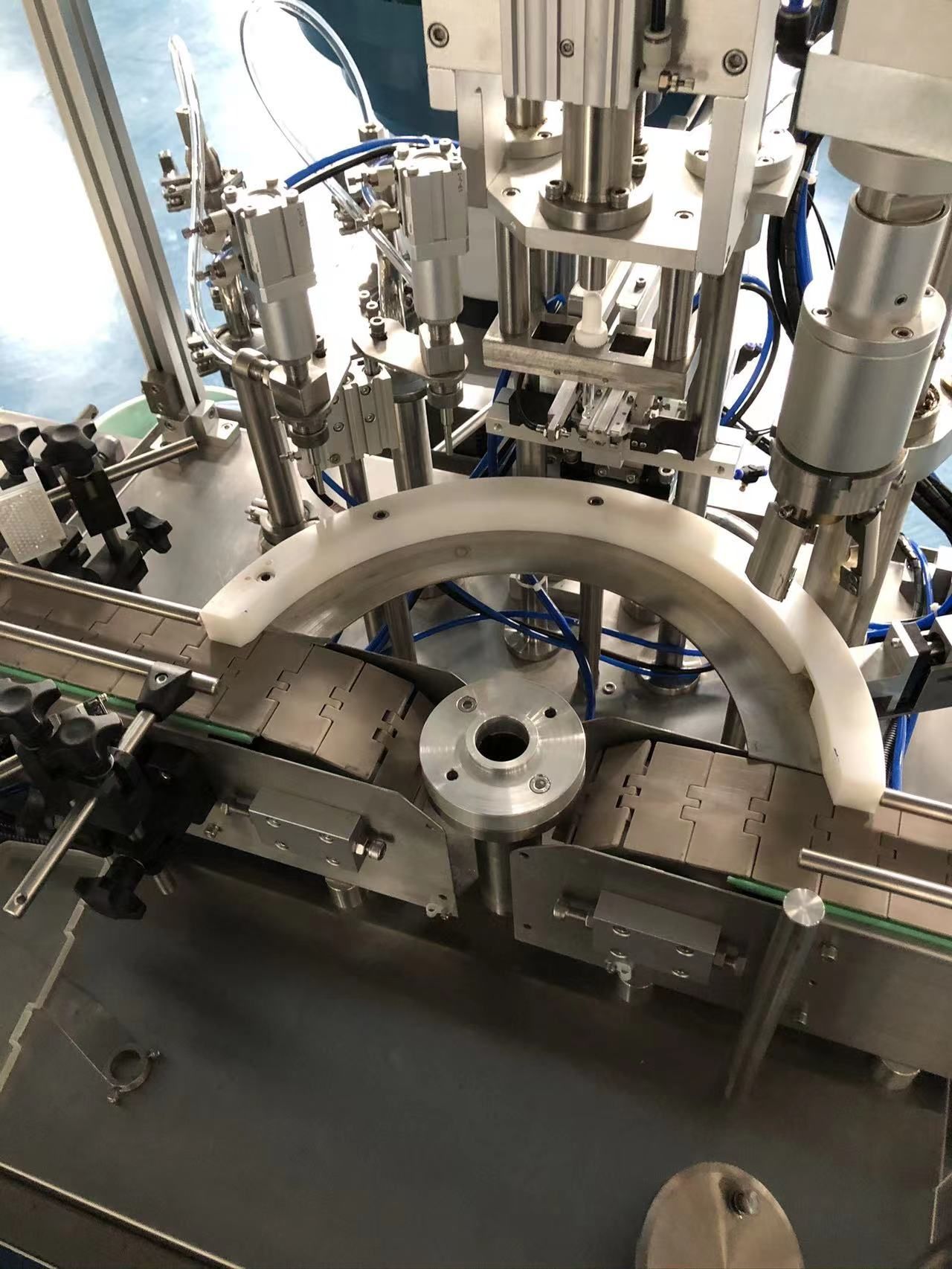 Automatisierte Maschine zum Befüllen von Flaschen auf einem Förderband. Weiße und silberne Komponenten mit blauen Schläuchen.