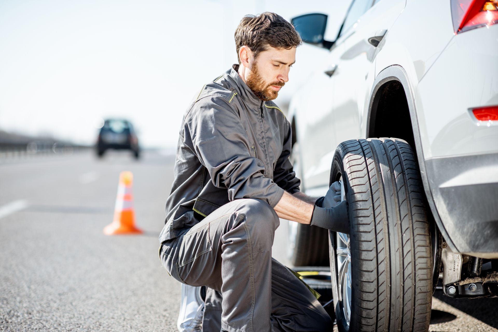 Un homme change un pneu sur une voiture blanche en bordure de route.