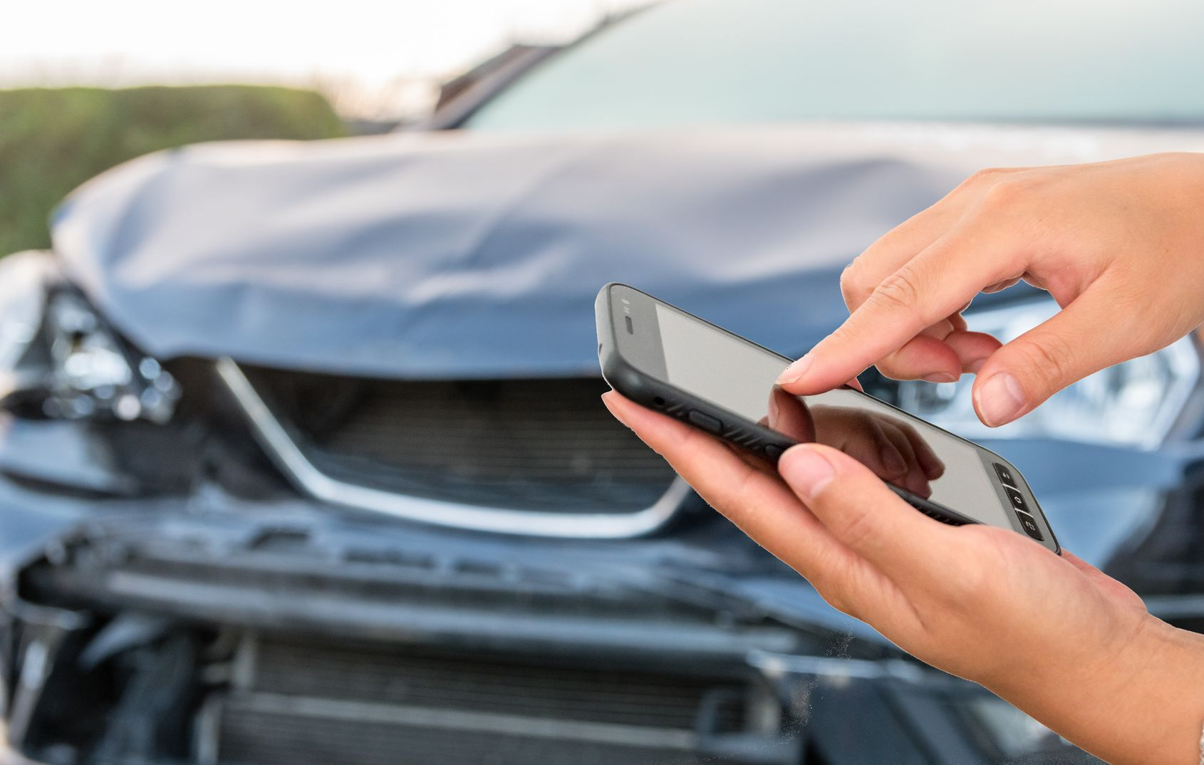 Une personne utilise son téléphone devant une voiture endommagée