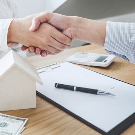 Un hombre le estrecha la mano a otro hombre delante de una casa modelo.