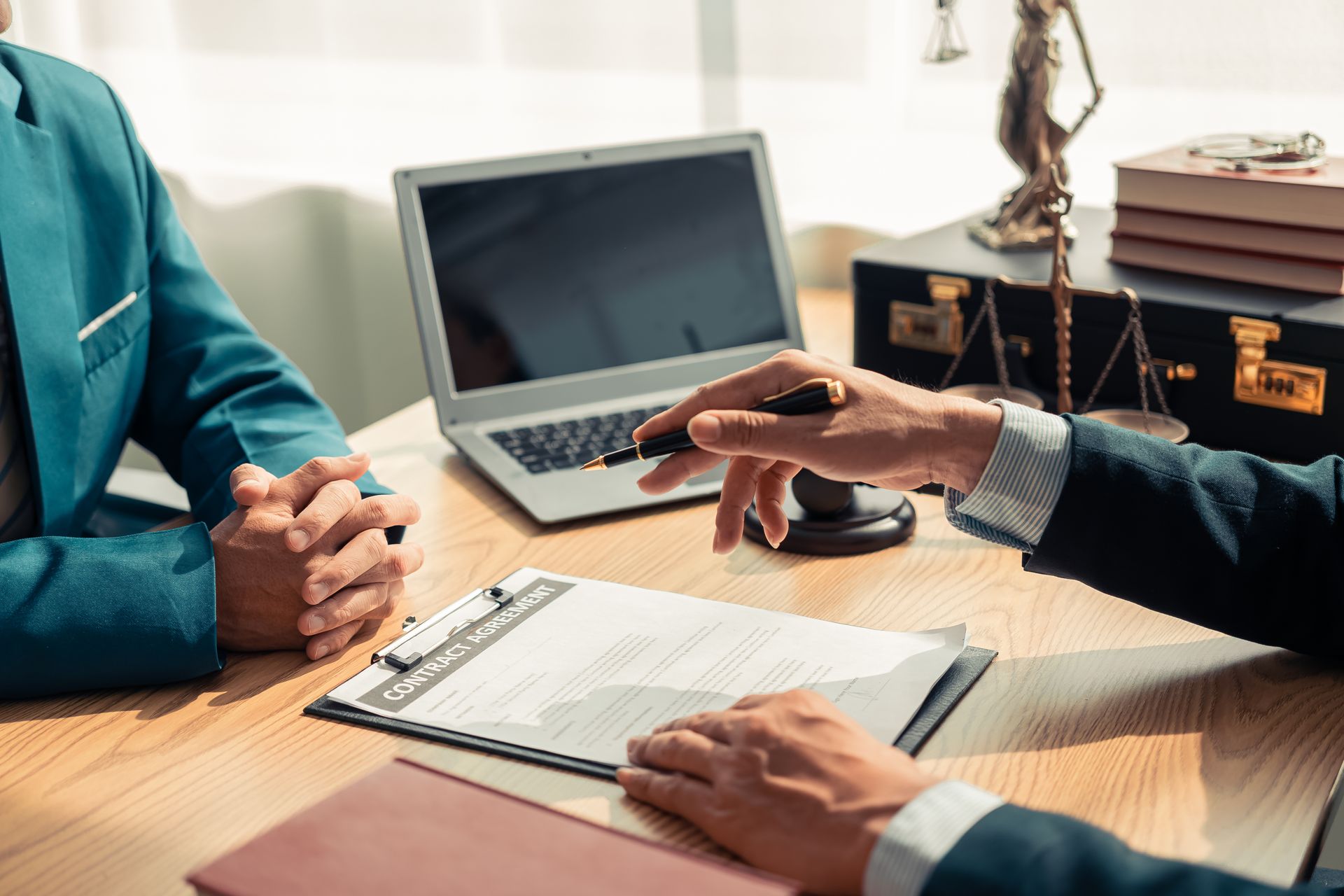 Deux personnes assises à un bureau examinent un document. Un ordinateur portable, une balance et des mallettes sont visibles en arrière-plan.