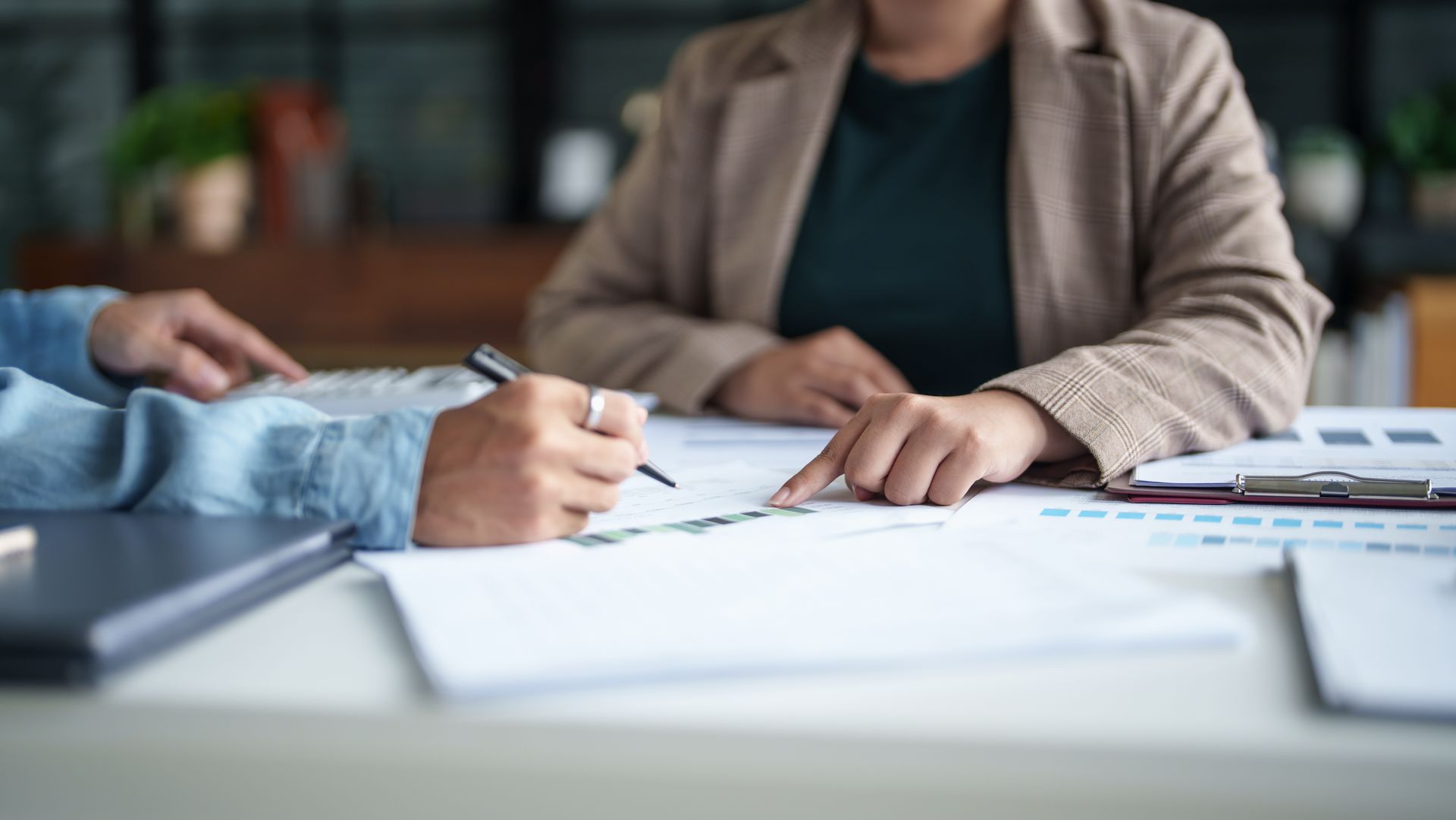 Deux personnes examinent des documents, l'une d'elles signant avec un stylo, assises à un bureau.