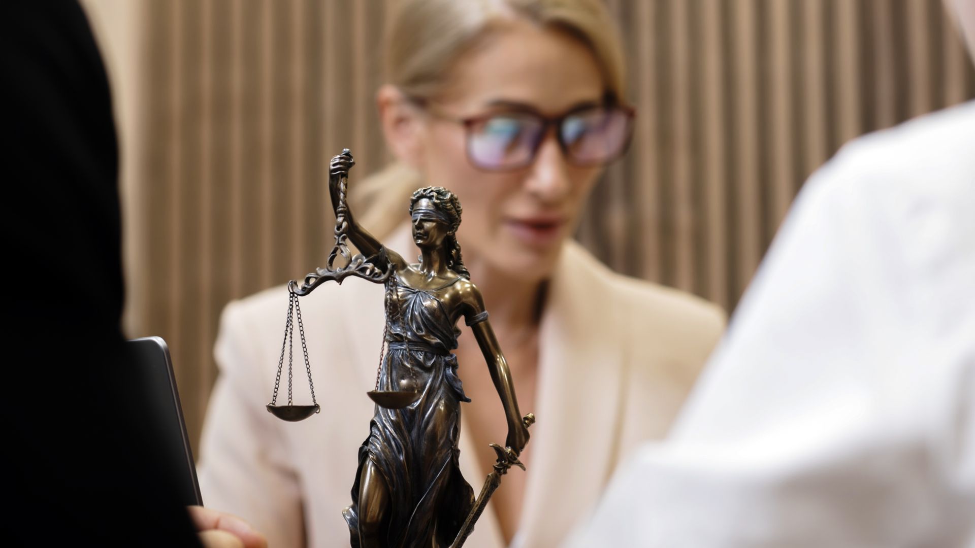 Statue de la Justice devant deux personnes, dont l'une porte des lunettes et un blazer.