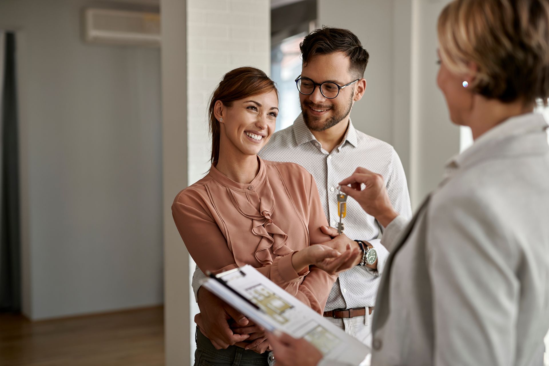 Un couple reçoit les clés de leur maison des mains d'un agent immobilier, tout sourire.