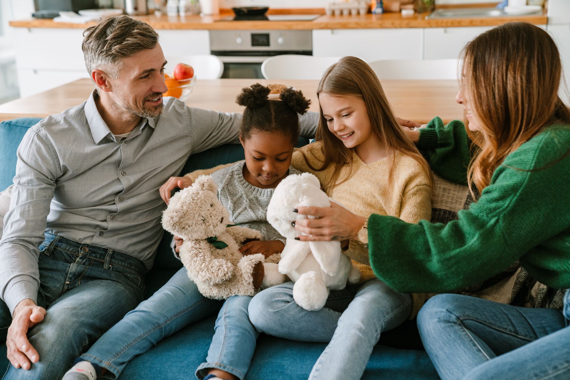 Une famille de quatre personnes assise sur un canapé, tenant des peluches et souriant à l'intérieur.