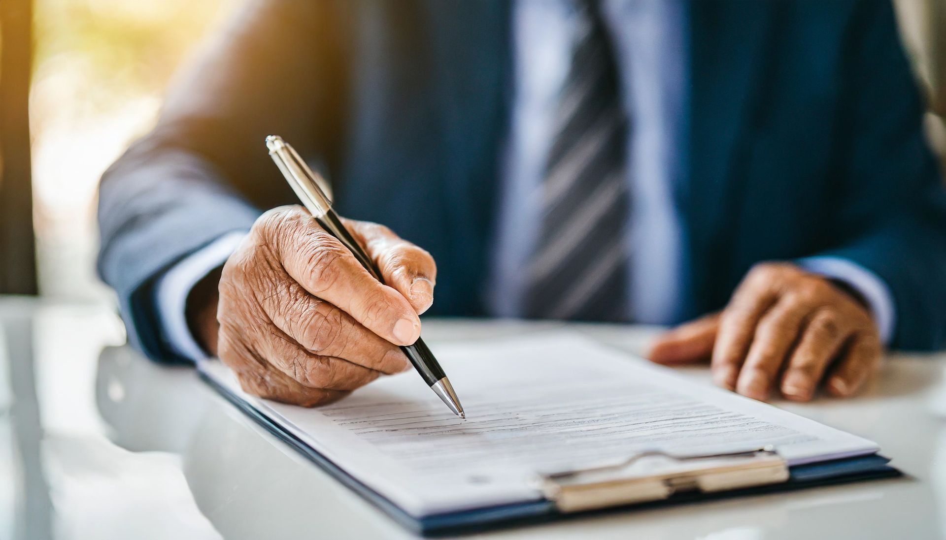 Une personne en costume signant un document sur un bloc-notes avec un stylo.