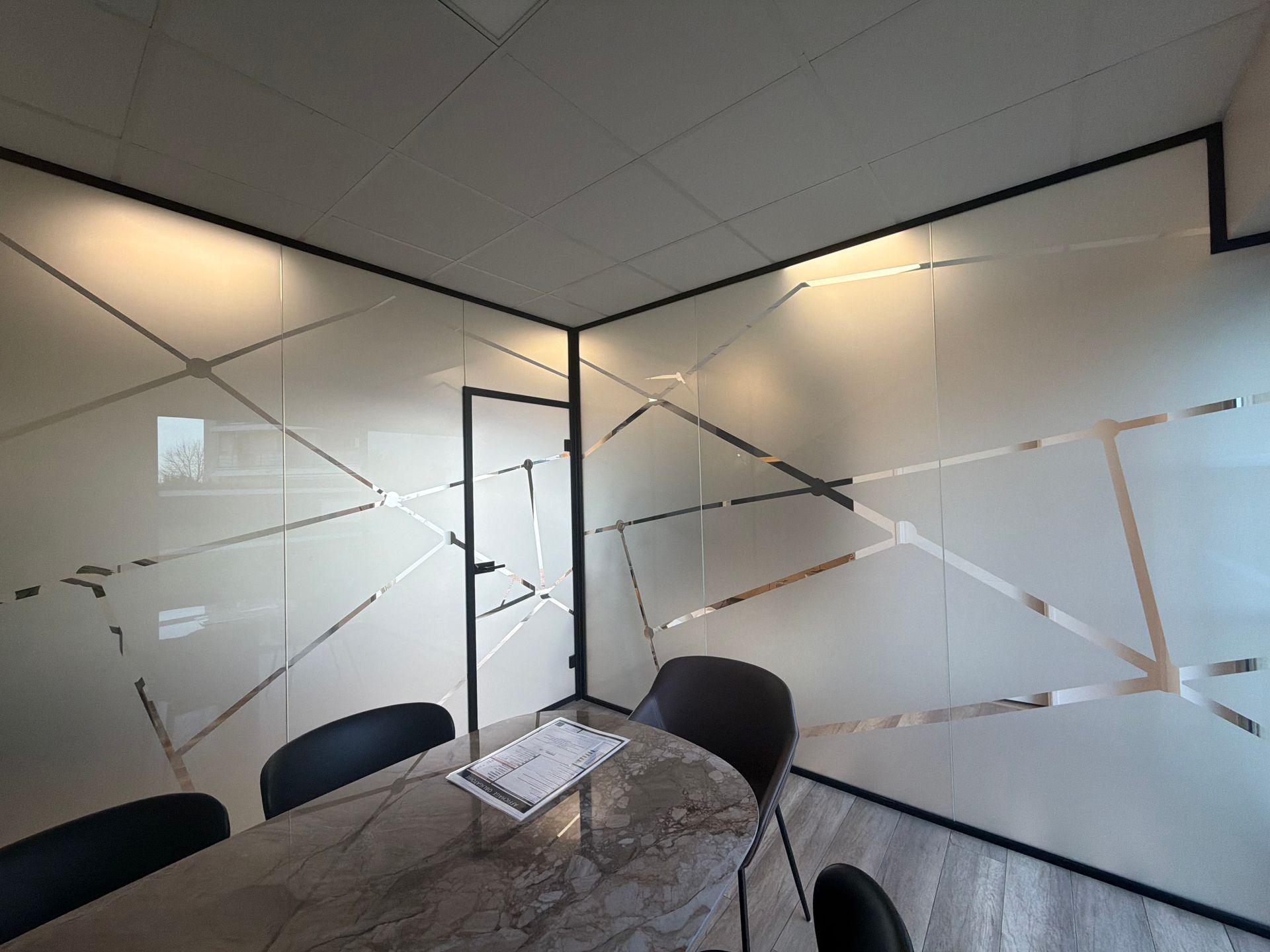 Salle de conférence avec parois en verre dépoli, motifs géométriques, table et chaises.