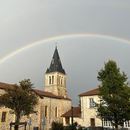 Église au clocher élancé sous un arc-en-ciel complet dans un ciel nuageux.