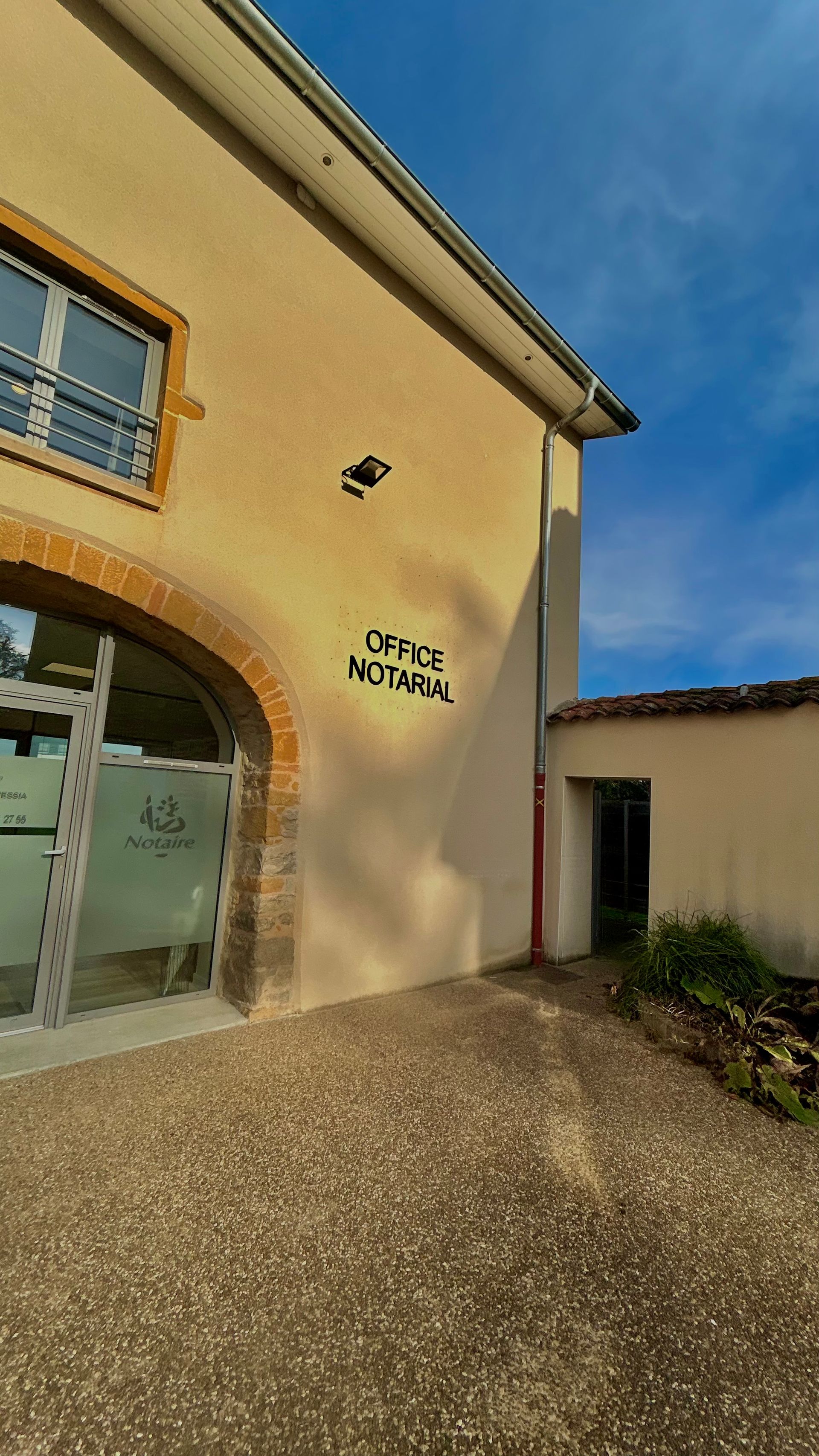 Immeuble beige avec fenêtre et porte cintrées, graffiti indiquant « Centre Résidence ». Ciel bleu.